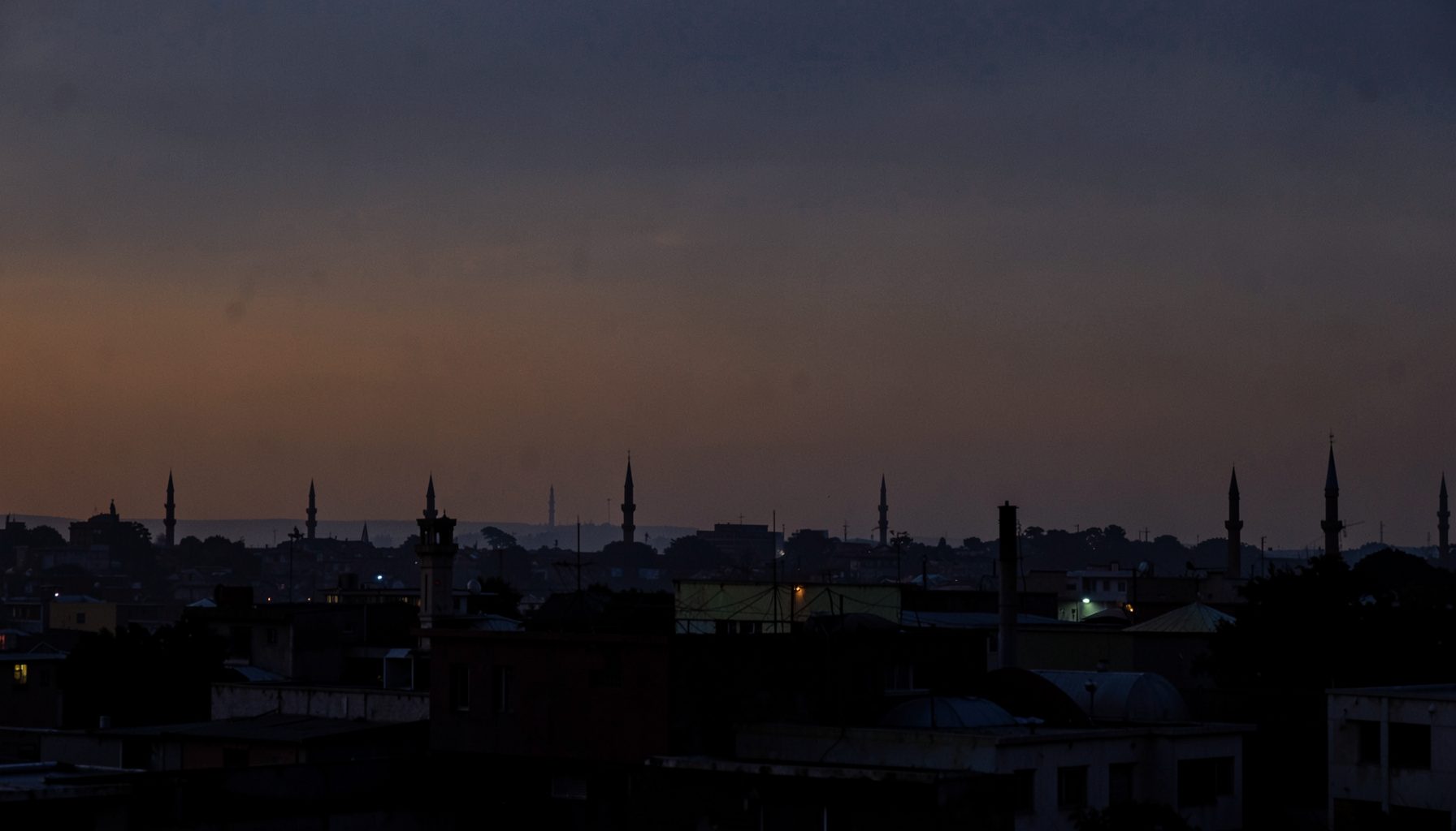 Warm dusky sky over a northern Nigerian cityscape, deep indigo and amber tones blending into a hazy horizon