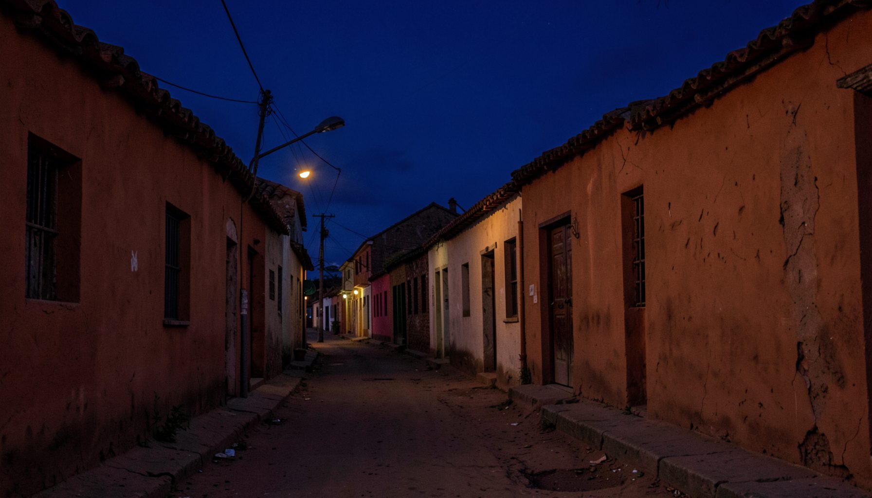 A quiet street in an old Kano neighbourhood at dusk, warm terracotta walls and deep indigo sky