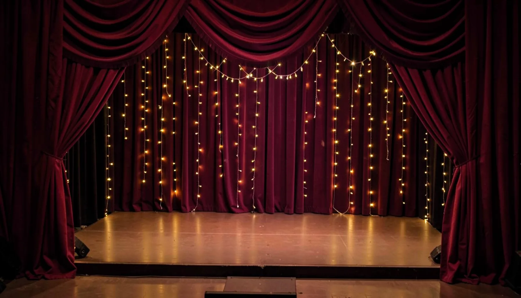 A glamorous Kannywood-style event backdrop with rich burgundy drapes and soft golden fairy lights, an empty stage awaiting performers